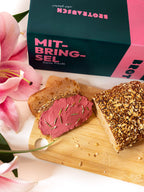 Mitbringsel Geschenkbox neben selbstgebackenem Brot und Blumen auf dem Tisch