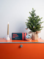Brotrausch Weihnachtsbox neben Kerze und kleinem Weihnachtsbaum auf einem orangefarbenen Sideboard