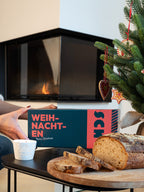 Hand nimmt die Brotrausch Weihnachtsbox am Kamin, davor selbst gebackenes Brot auf einem Holzbrett