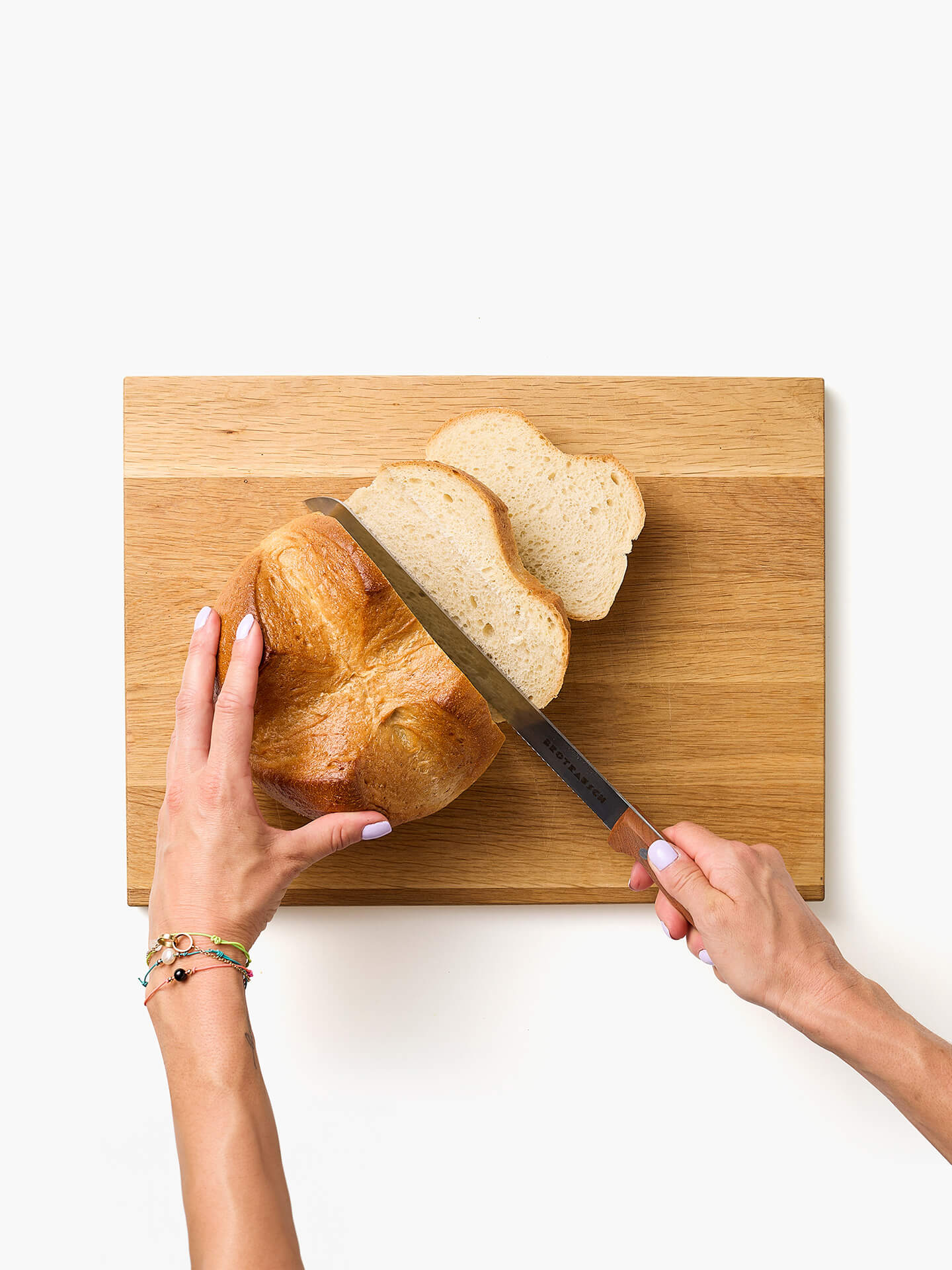 Frisches Brot wird auf einem Holzbrett mit dem Brotrausch Brotmesser in Scheiben geschnitten